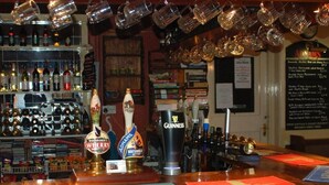 A bar area with multiple beer taps, shelves of bottles, and a menu board. - The Theberton Lion (Leiston)