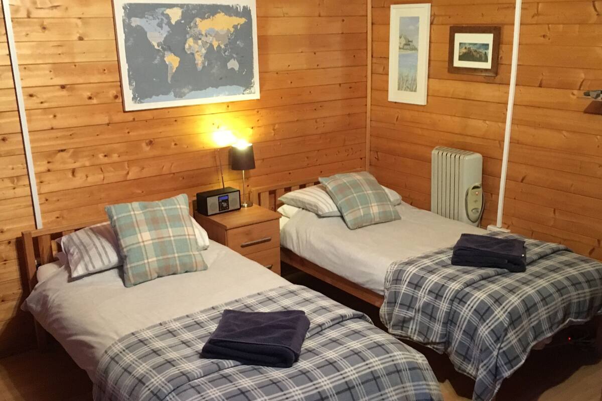 A wooden cabin room with two beds, a world map, and a framed picture on the wall.