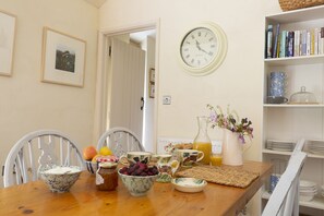 En matplats med ett träbord dukat för frukost, med skålar fyllda med frukt, en kanna med juice och en vas med blommor.