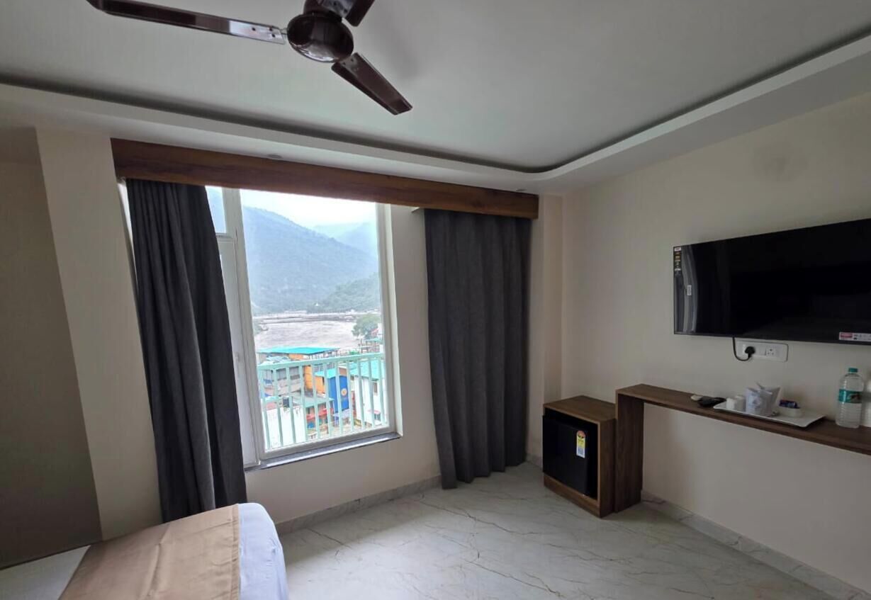 A hotel room with a Galaxy S25 Ultra bed, a TV, a wooden TV stand, and a window with curtains.
