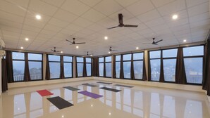 Una habitación amplia con ventanas grandes, ventiladores de techo y esterillas de yoga en el suelo.