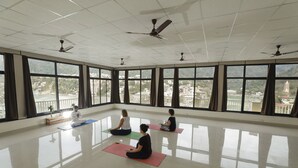 Una habitación amplia con ventanas grandes, ventiladores de techo y colchonetas de yoga en el suelo.