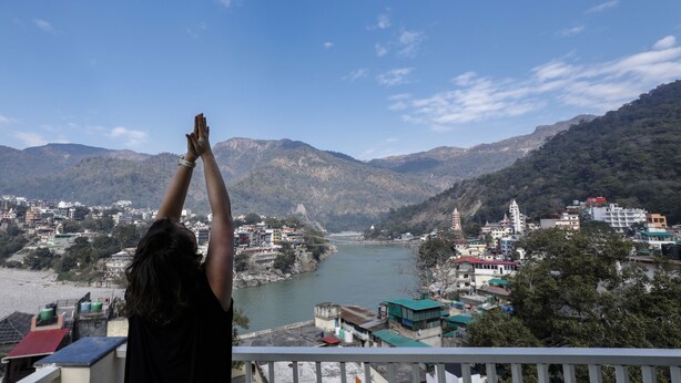 Una persona en un balcón con vistas a un río, montañas y un pueblo.