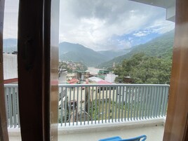 A balcony with a view of a mountainous landscape, a river, and a distant temple.