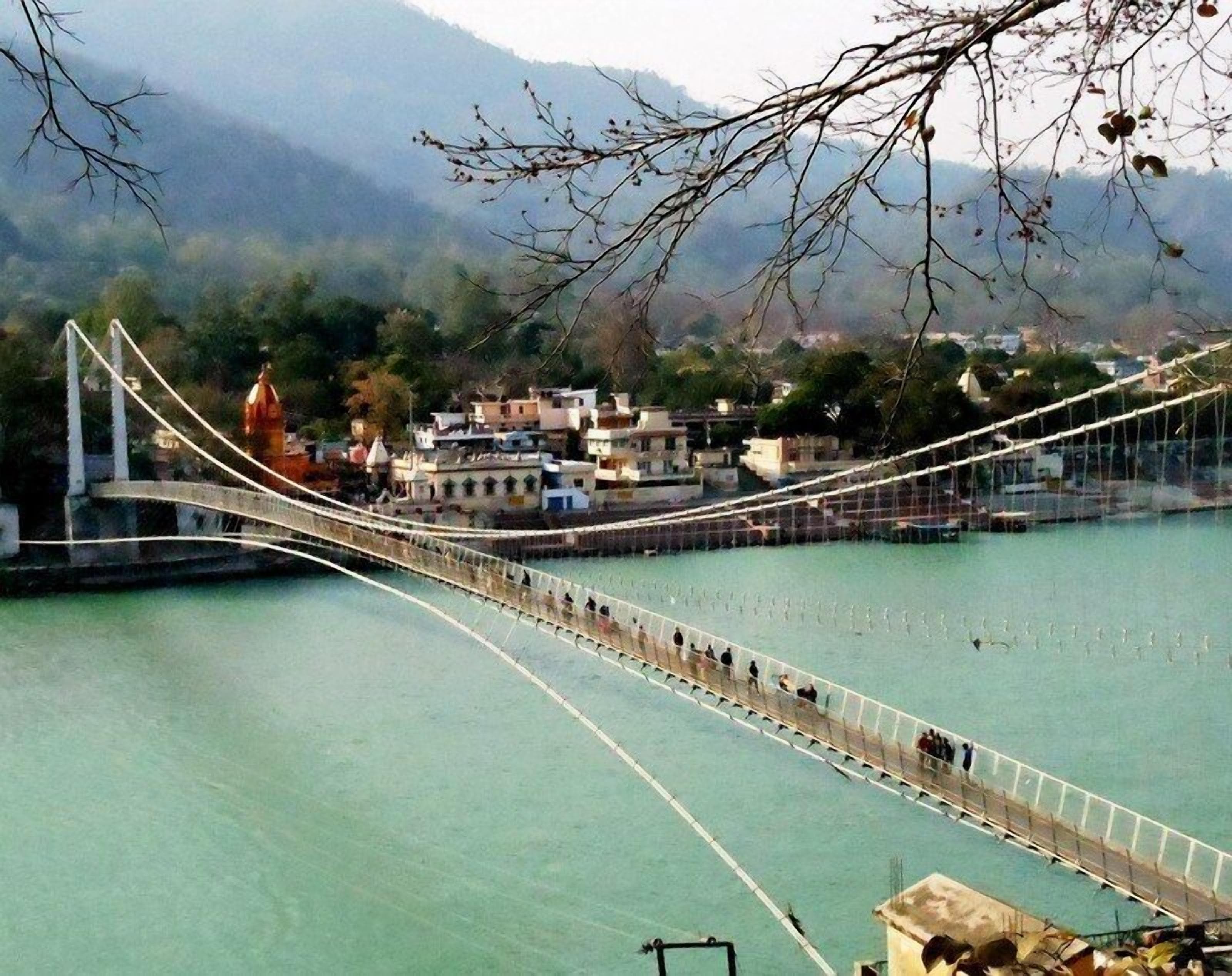 Un puente colgante sobre una masa de agua con edificios al fondo.