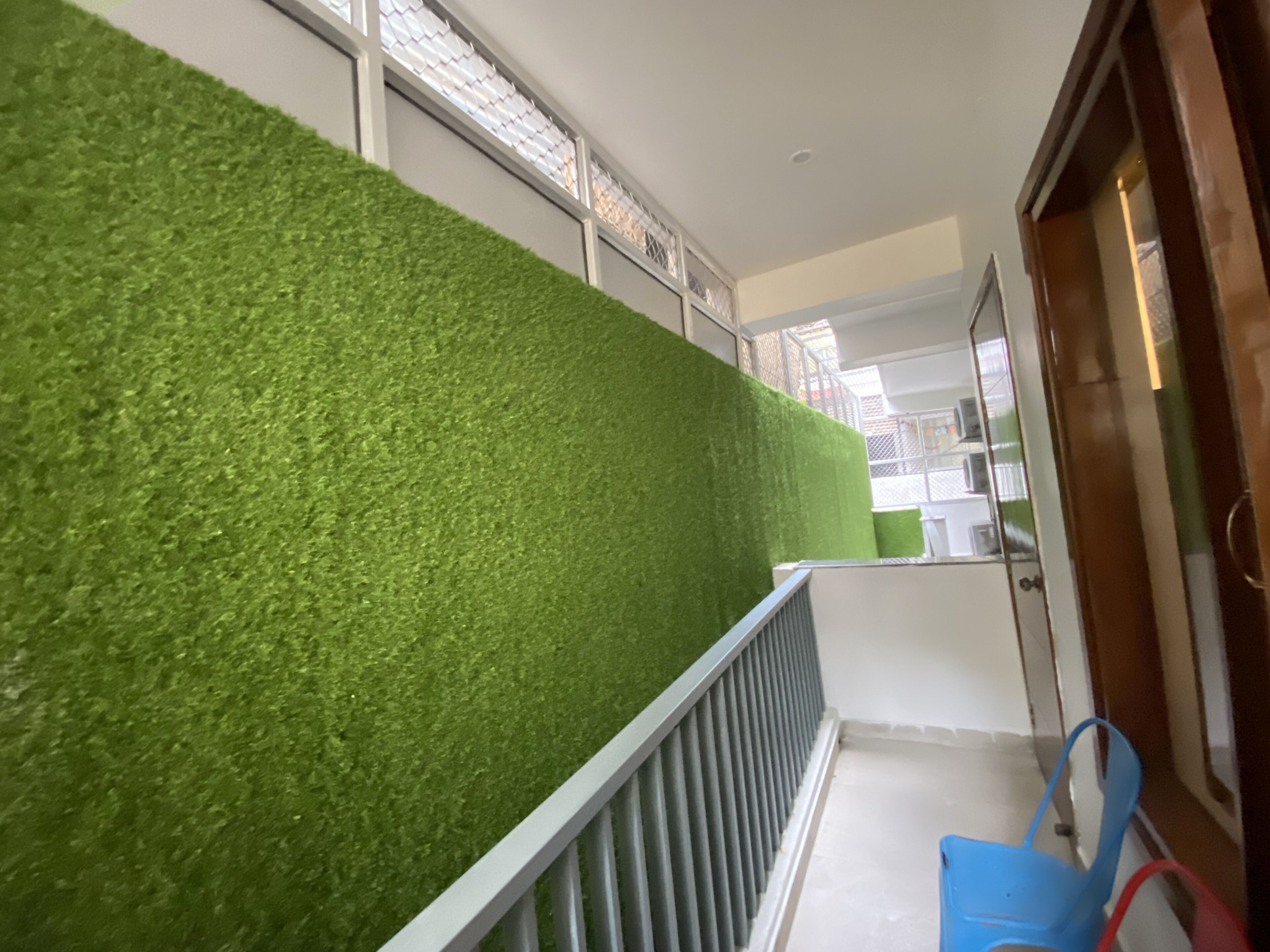 A hallway with a green artificial grass wall, a metal railing, and a blue chair.