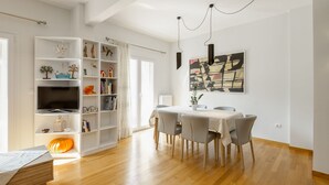 A modern living room with a dining area, wooden flooring, and a large bookshelf filled with decorative items.