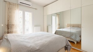 A bedroom with a large bed, a wardrobe, a mirror, and a window with curtains.