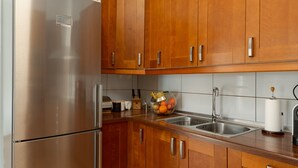 A kitchen with wooden cabinets, a stainless steel refrigerator, a double sink, and a wooden countertop.