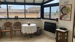 Un solarium con piso de baldosas, una mesa redonda con mantel blanco, dos sillas de mimbre, un televisor y una estantería.