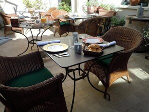 Un coin repas avec des meubles en osier, une table dressée avec des assiettes, des verres et un panier de pain.