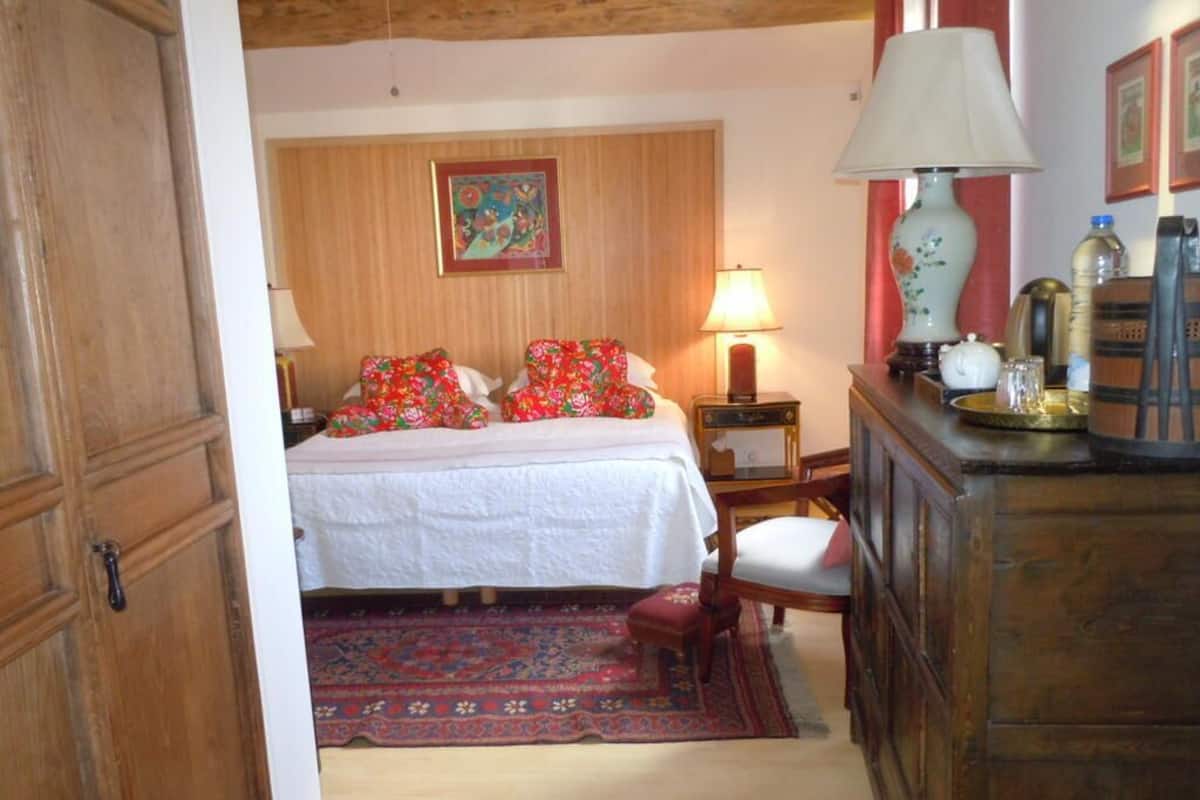 Un dormitorio con cama, mesita de noche, lámpara, silla, cómoda y alfombra.