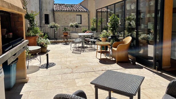 Un patio con mobiliario exterior, una parrilla y plantas en macetas.