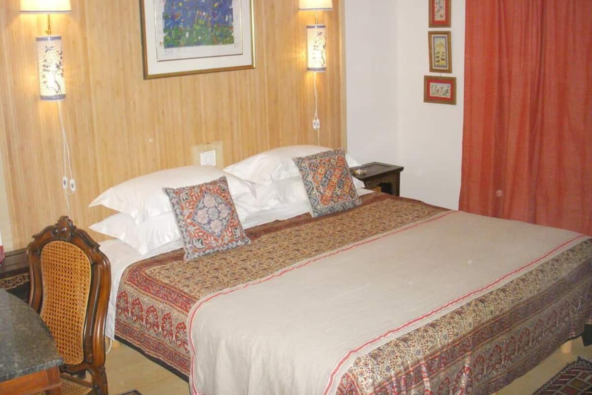 Habitación de hotel con una cama grande, dos lámparas de pared, un cuadro enmarco y una cortina roja.