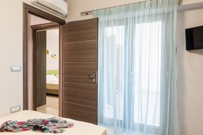A bedroom with a wooden wardrobe, a bed with a white headboard, and a window with a sheer curtain. - Bright Modern Flat next to Beach (Platanias)