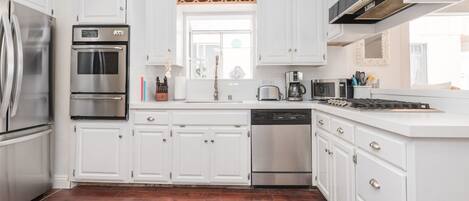 Una cocina moderna con armarios blancos, electrodomésticos de acero inoxidable y piso de madera.