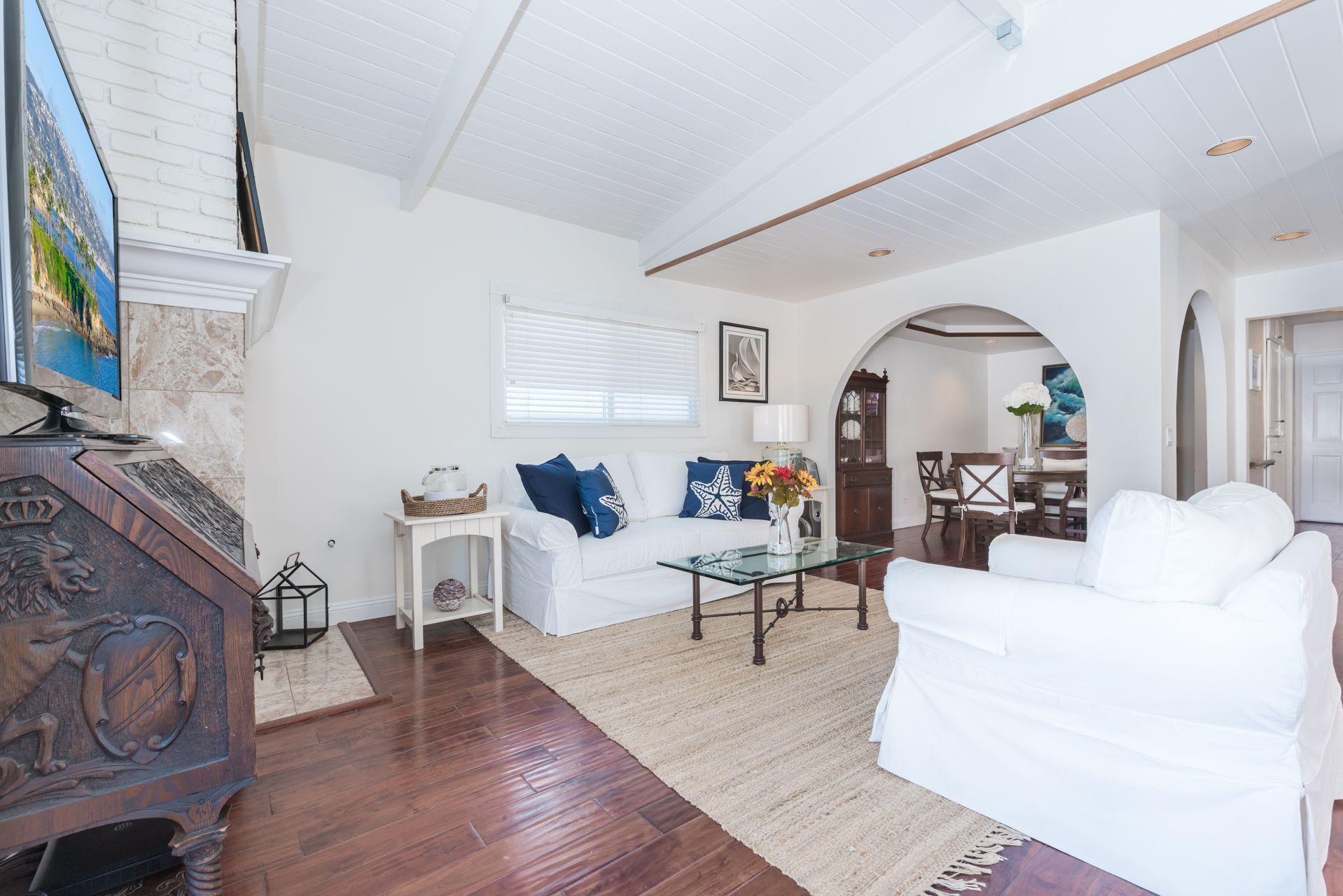 Amplia sala de estar con un sofá blanco, una mesa de centro de vidrio y un mueble de entretenimiento de madera.