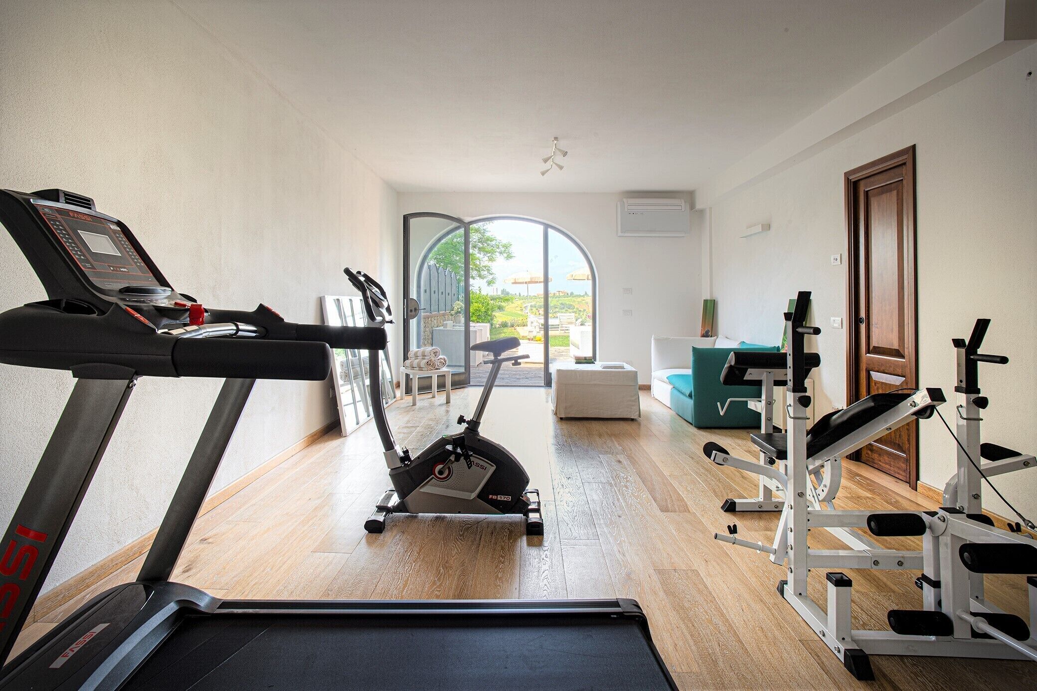 Un gimnasio en casa con cinta de correr, elíptica y banco para pesas.