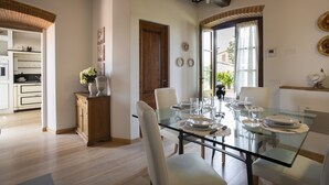 A dining area with a glass table set for six, surrounded by white chairs. A wooden cabinet with a vase of flowers is to the left. - Private house in the Chianti area for 12 persons, pool and A / C (Tavarnelle Val di Pesa)