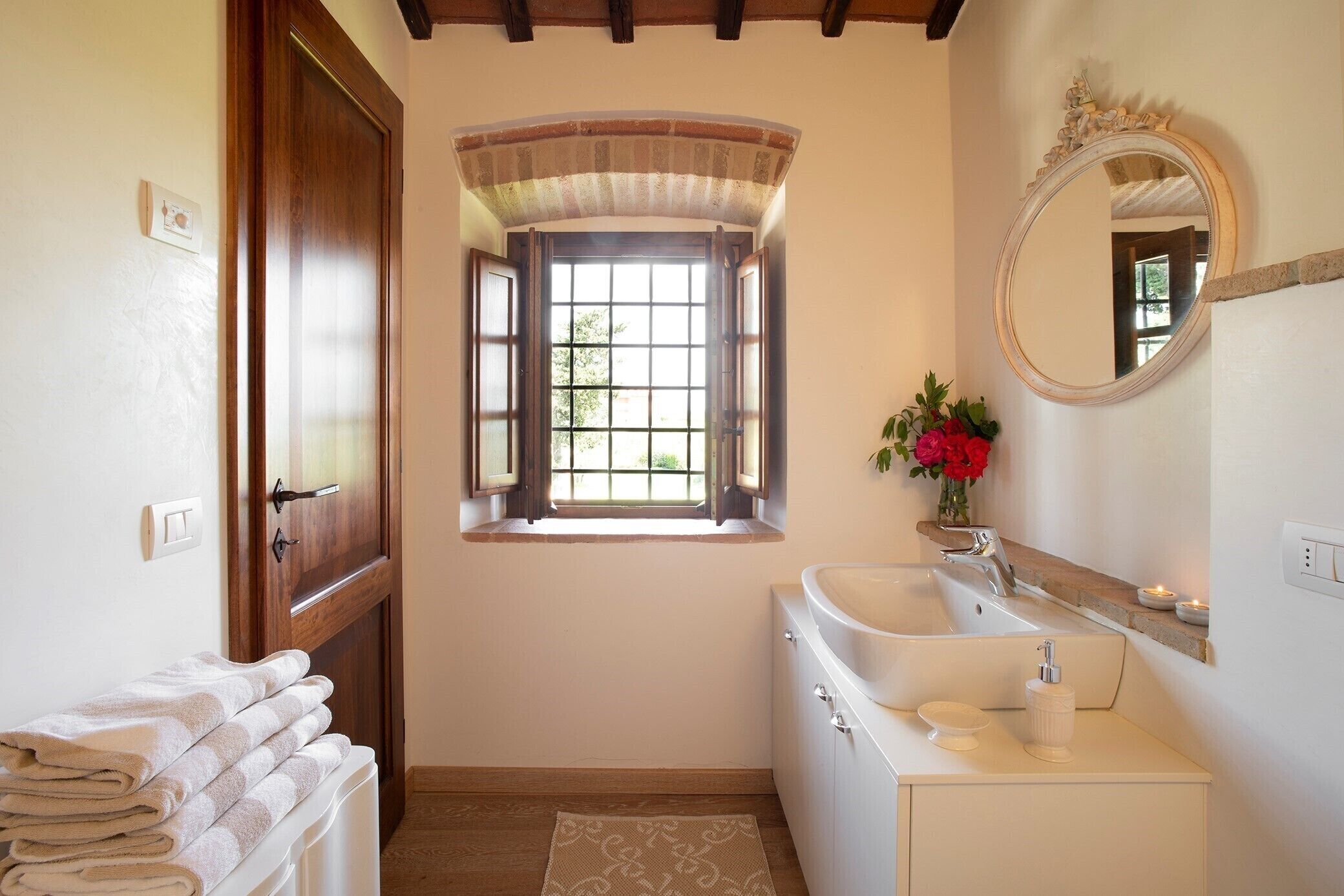 A bathroom with a window, a sink, a mirror, and towels.