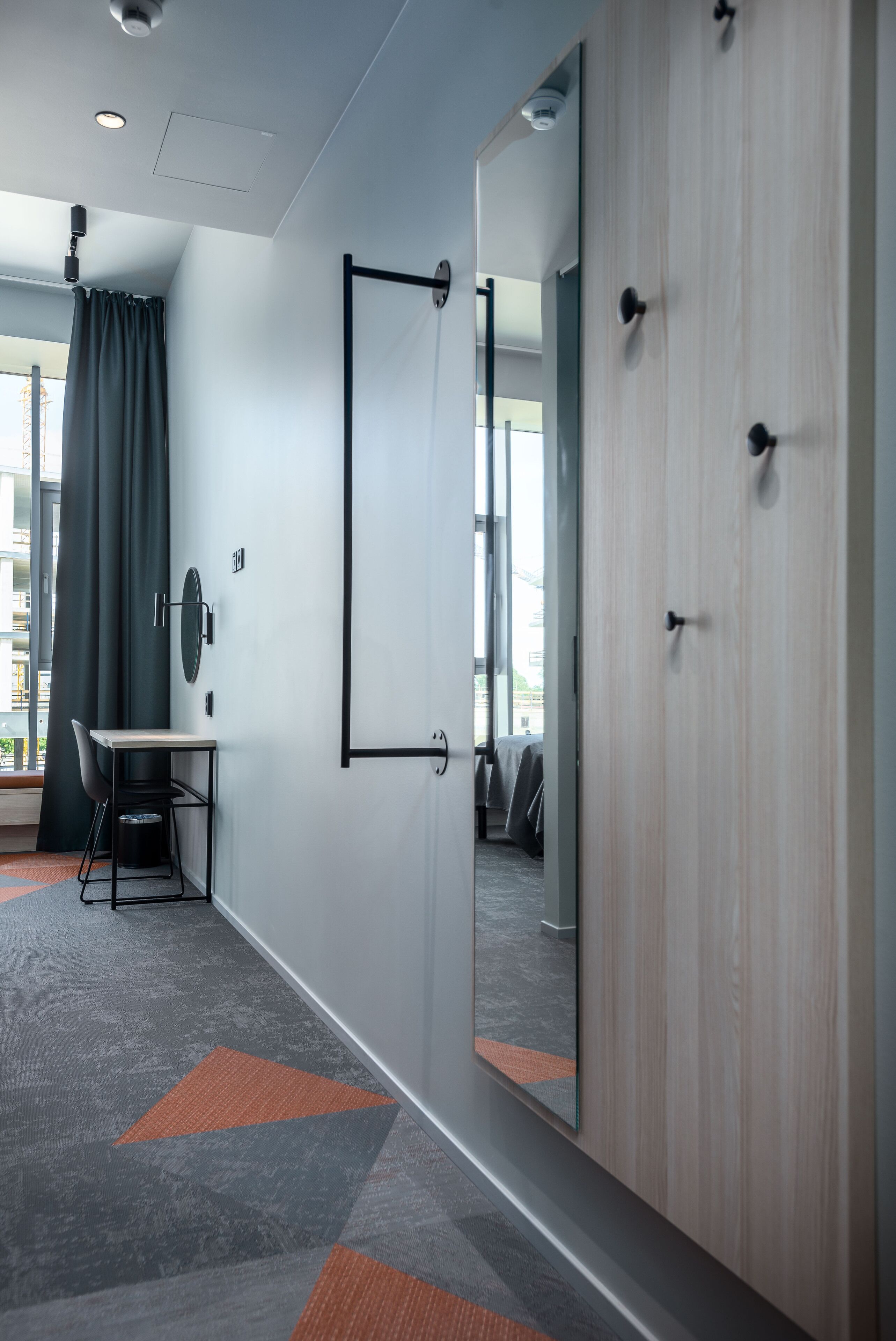 A modern hotel room with a desk, chair, and a large mirror.