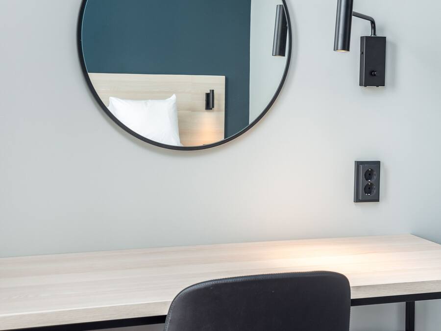 A modern room with a round mirror on the wall, a desk with a chair, and a wall-mounted lamp.