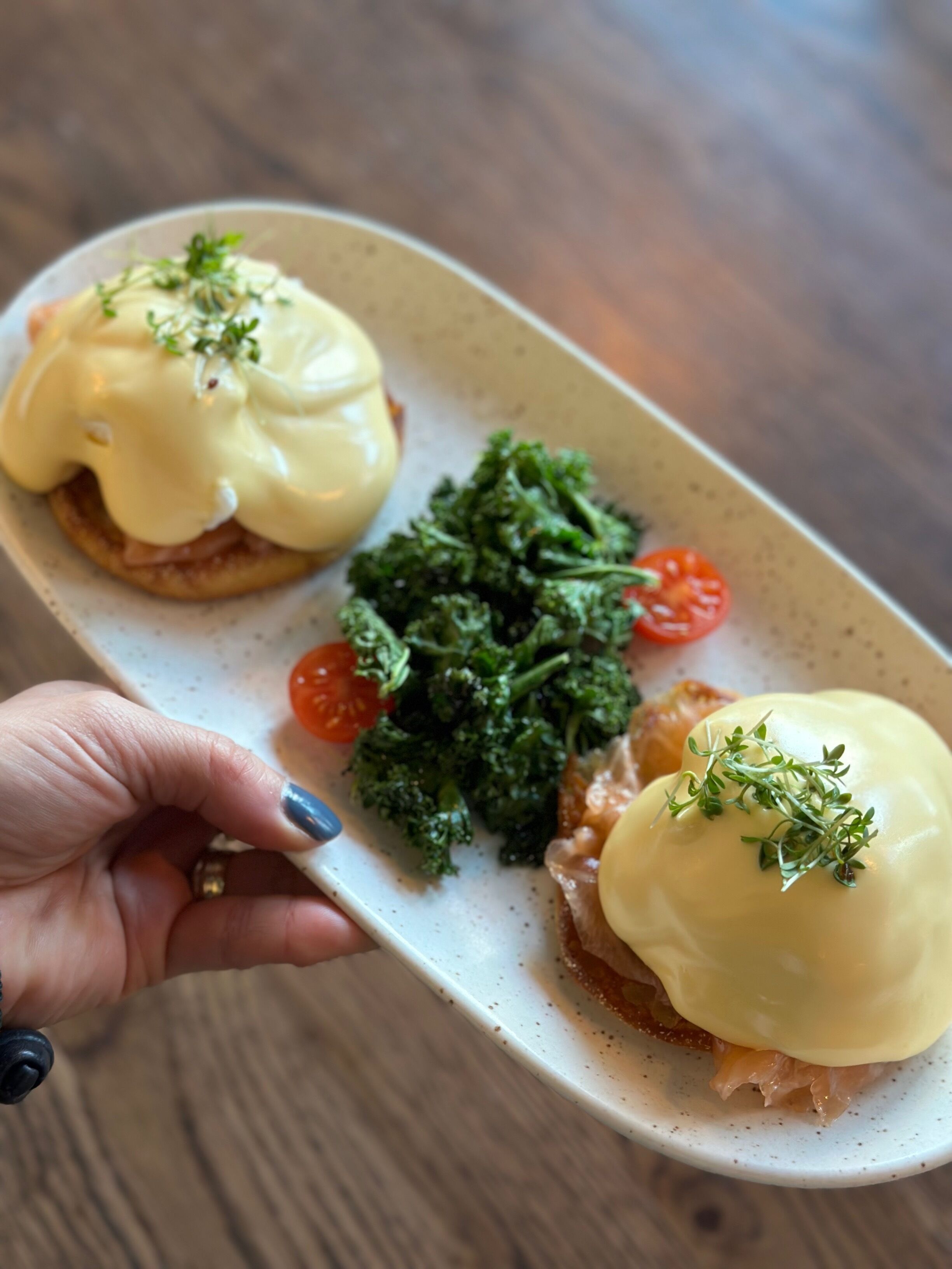 Een bord met eggs benedict, boerenkool en kerstomaatjes.