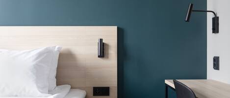 Una habitación de hotel moderna con cabecera de madera, mesita de noche, escritorio y silla.