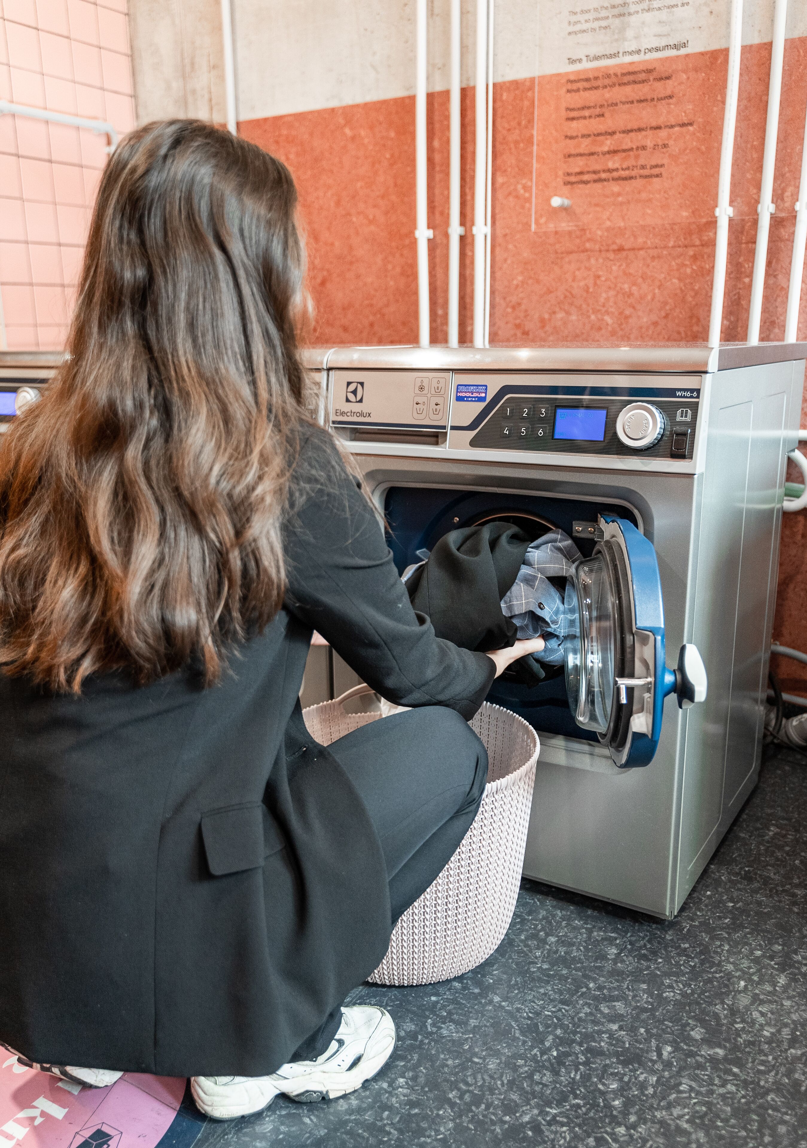 A person loading a washing machine with a basket of clothes.
