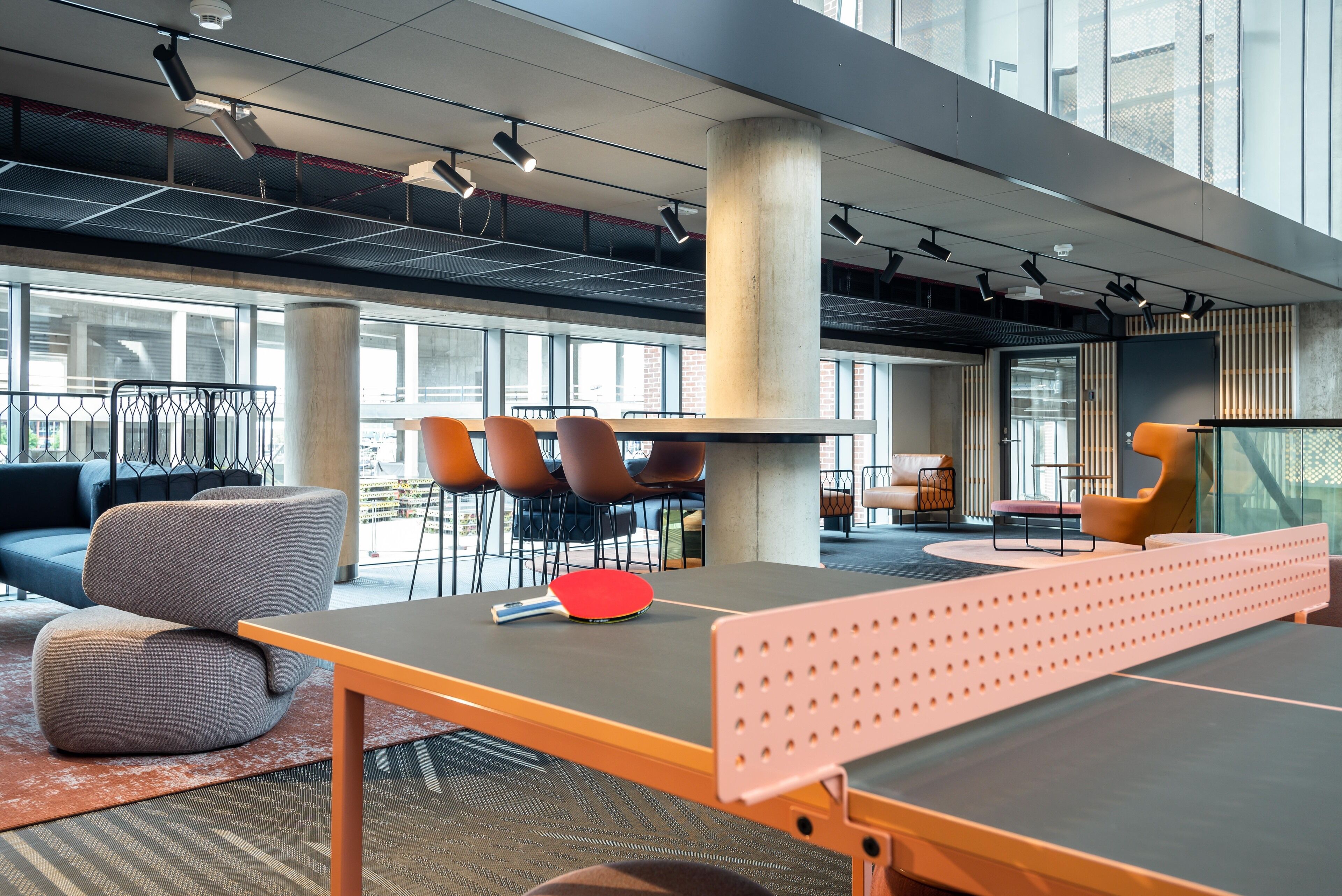 A modern indoor space with a ping pong table, seating, and large windows.
