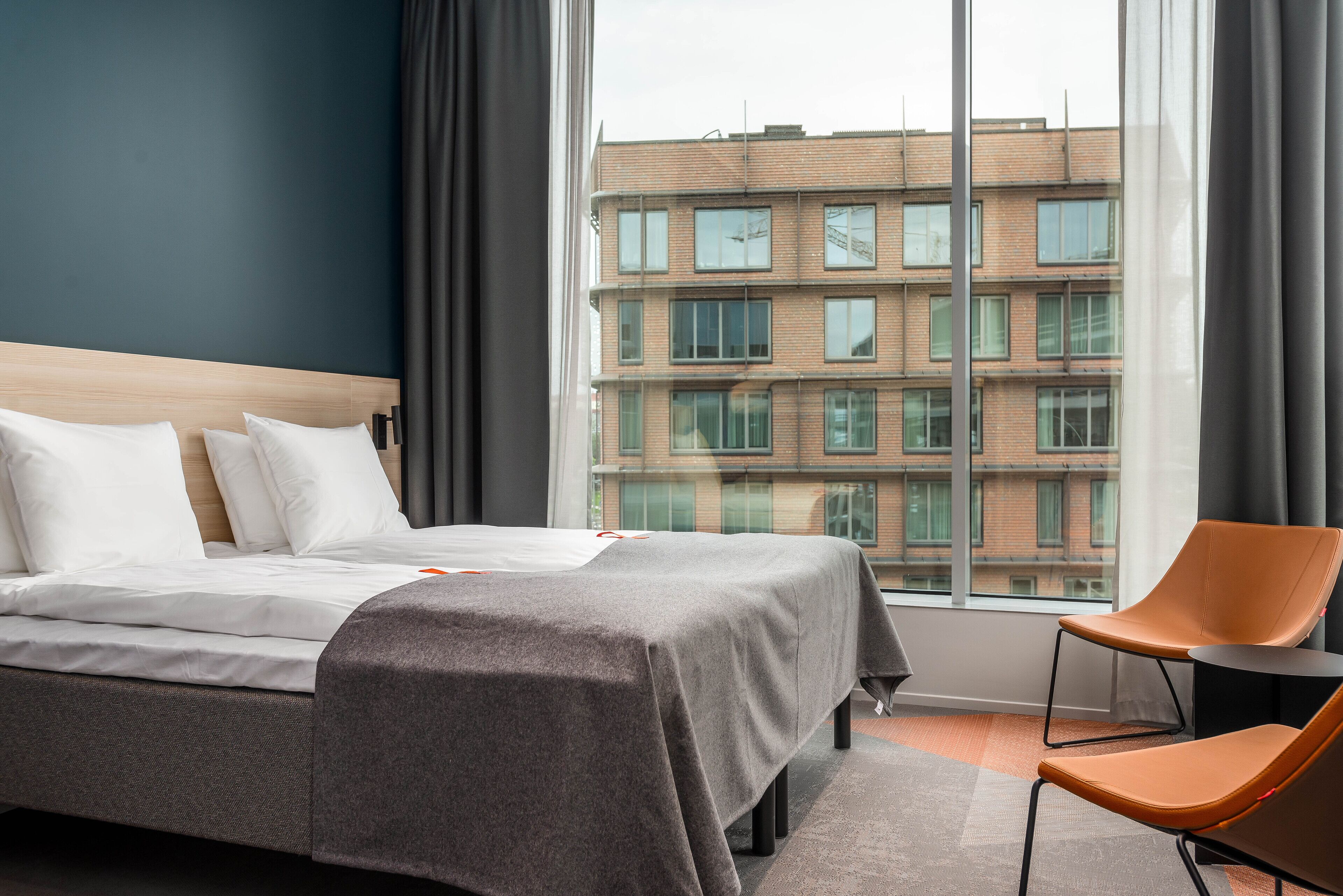 A hotel room with a large bed, a chair, and a view of a building through a window.
