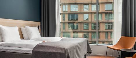 A hotel room with a large bed, a chair, and a view of a building through a window.