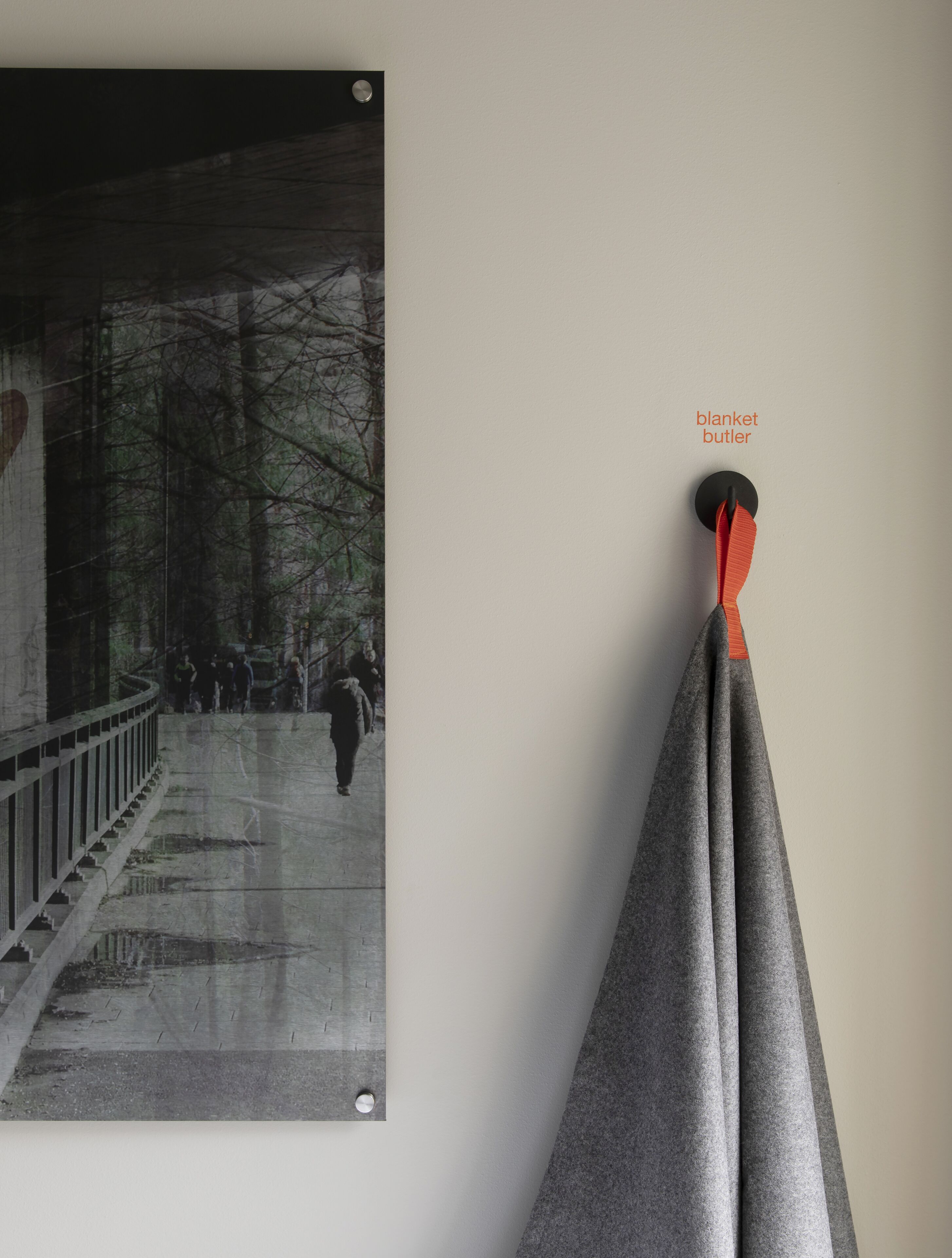 A photograph of a bridge with people walking on it, mounted on a wall next to a grey blanket and a black object labeled "blanket butler".