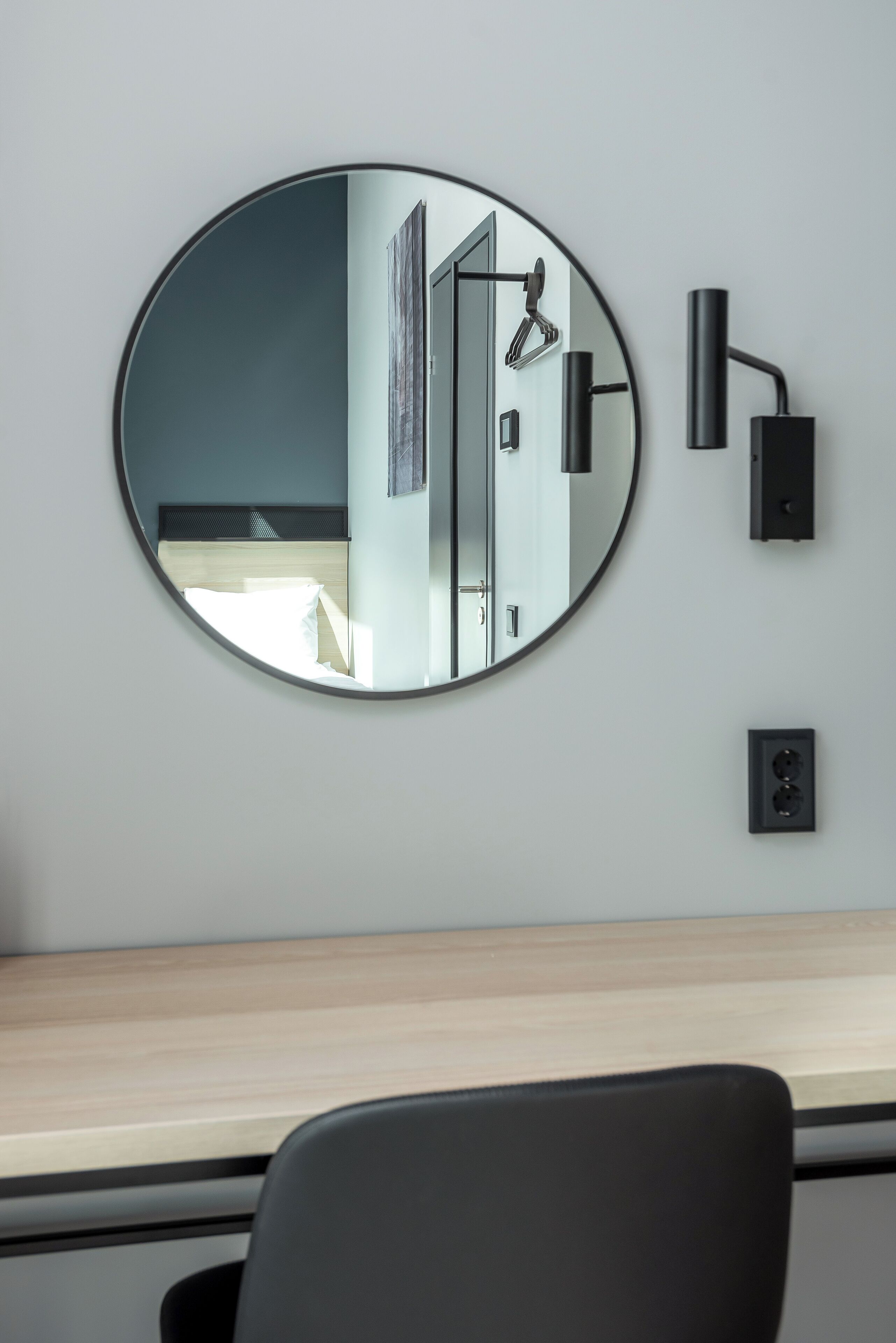 A round mirror on a wall, a black desk, and a black chair.