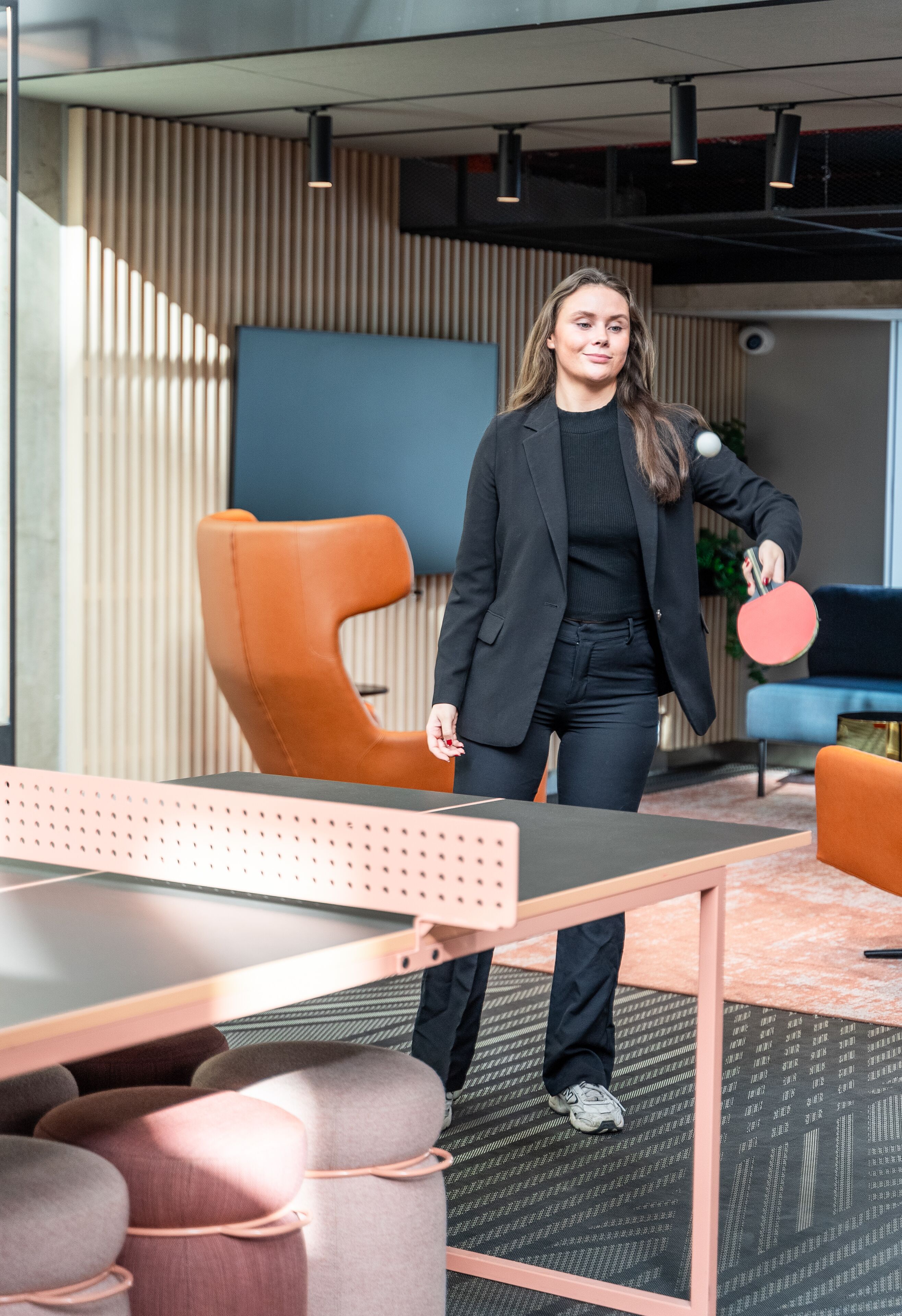 A modern office space with a ping pong table, a large orange chair, and a blue sofa.