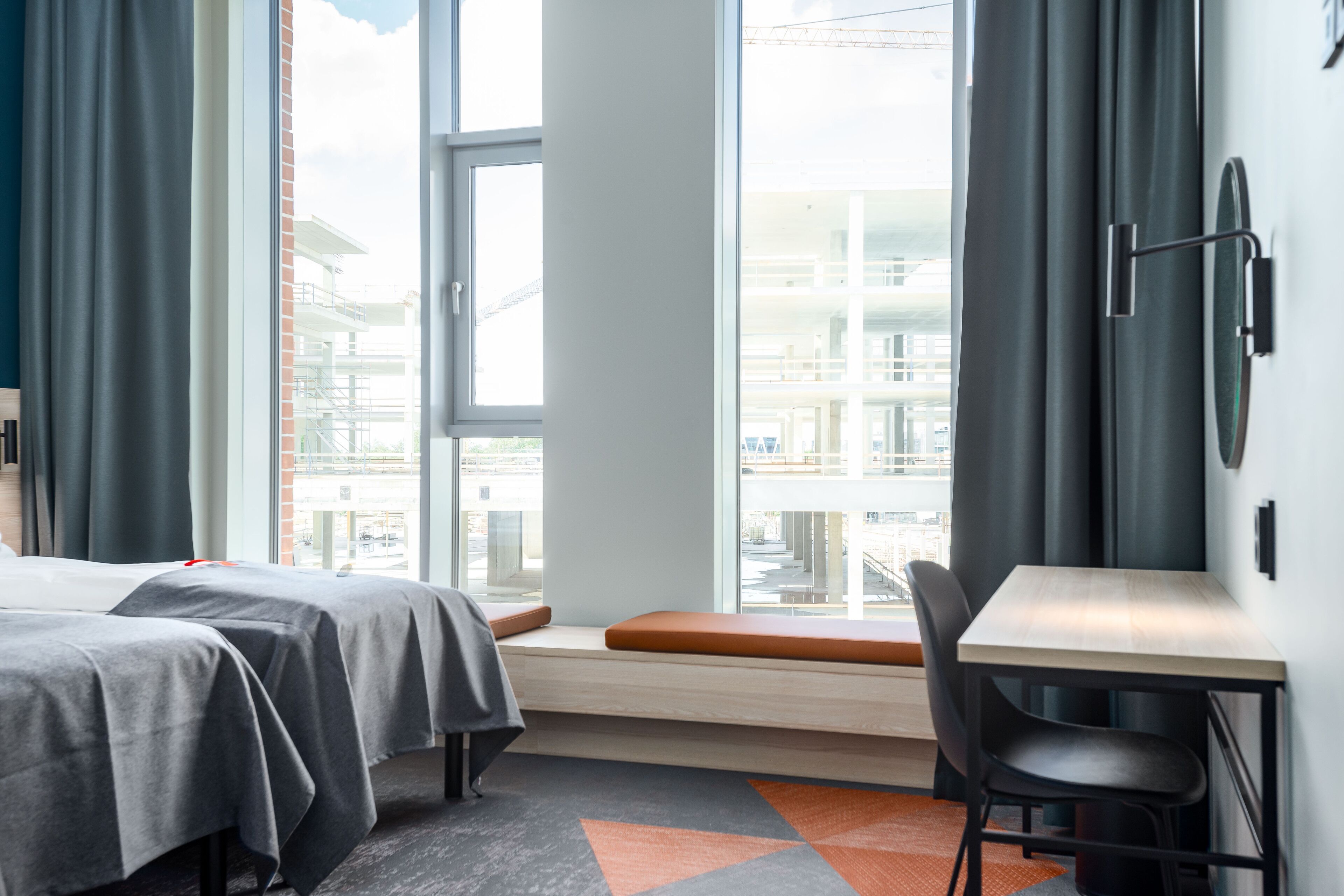 Ett hotellrum med två sängar, ett skrivbord och ett fönster med utsikt över byggnader.