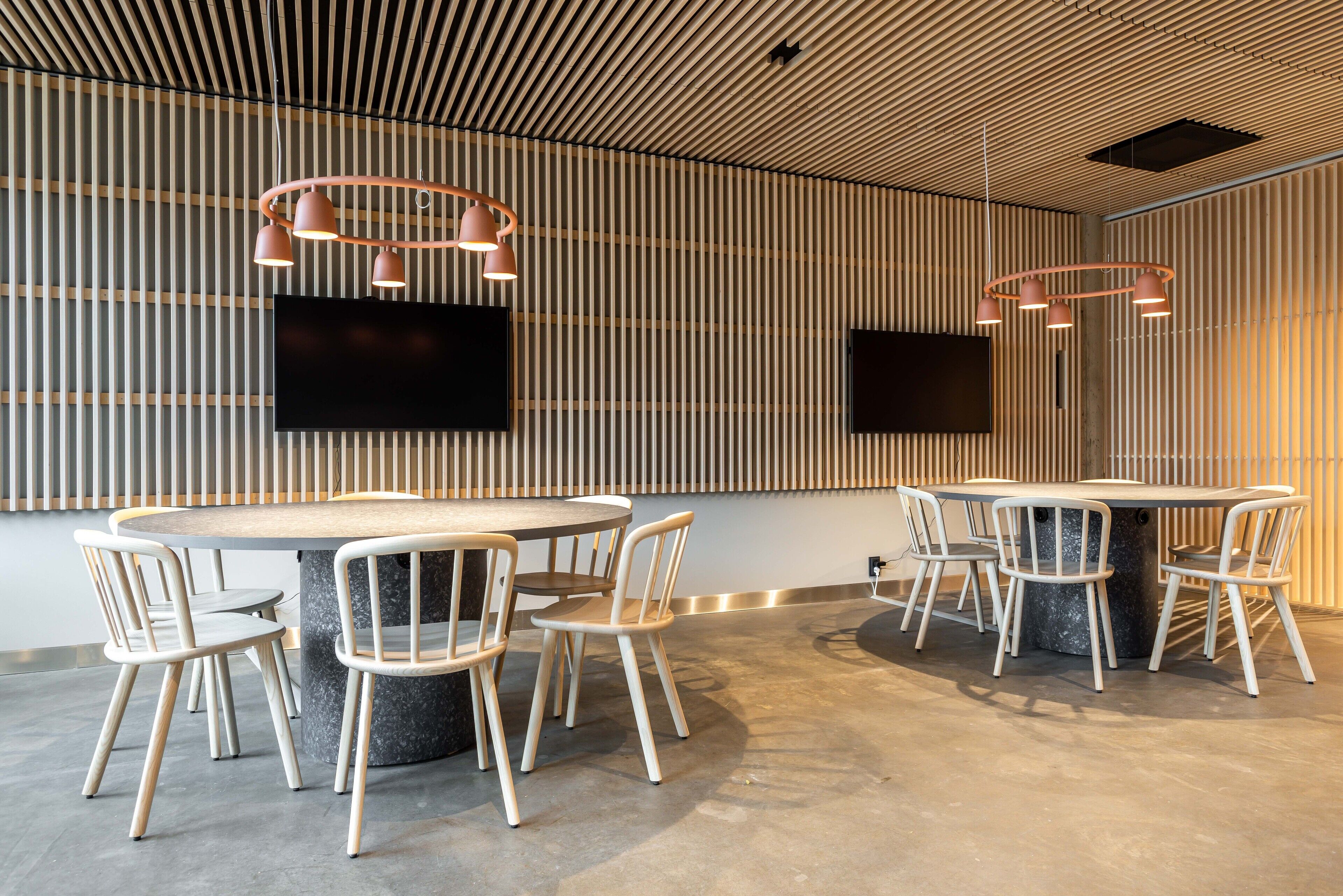 Une salle de conférence moderne équipée d’une table ronde, de six chaises et de deux lampes suspendues.