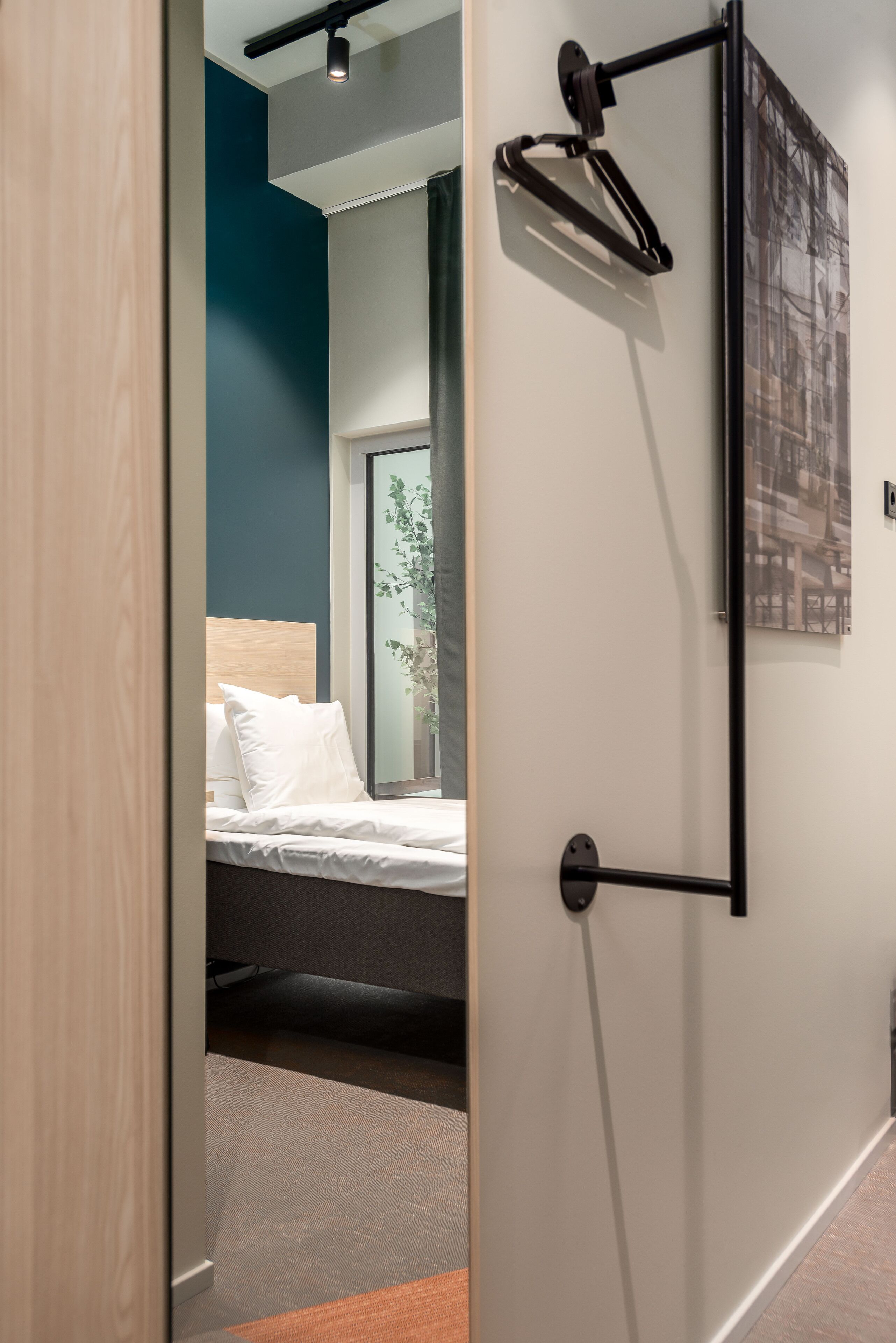 A modern hotel room with a bed, a window, a wall-mounted light fixture, and a framed picture.