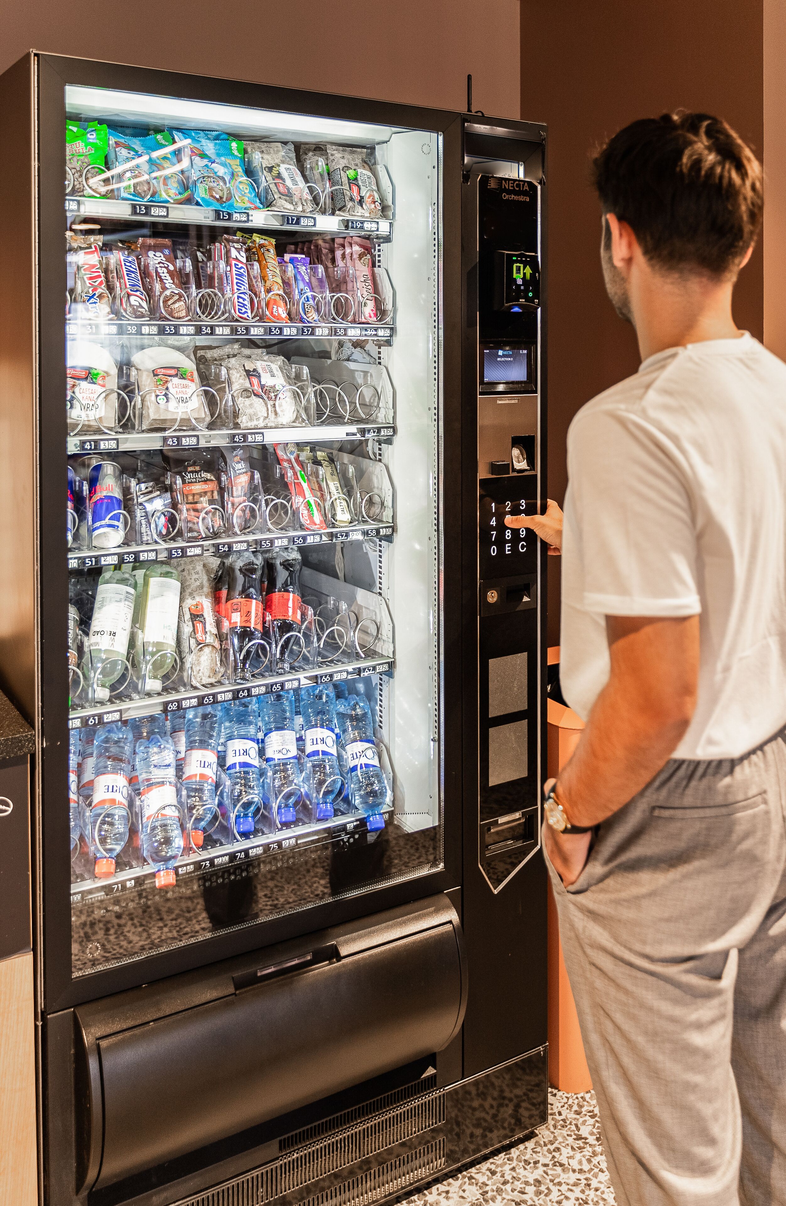 A person interacting with a vending machine stocked with various snacks and drinks.