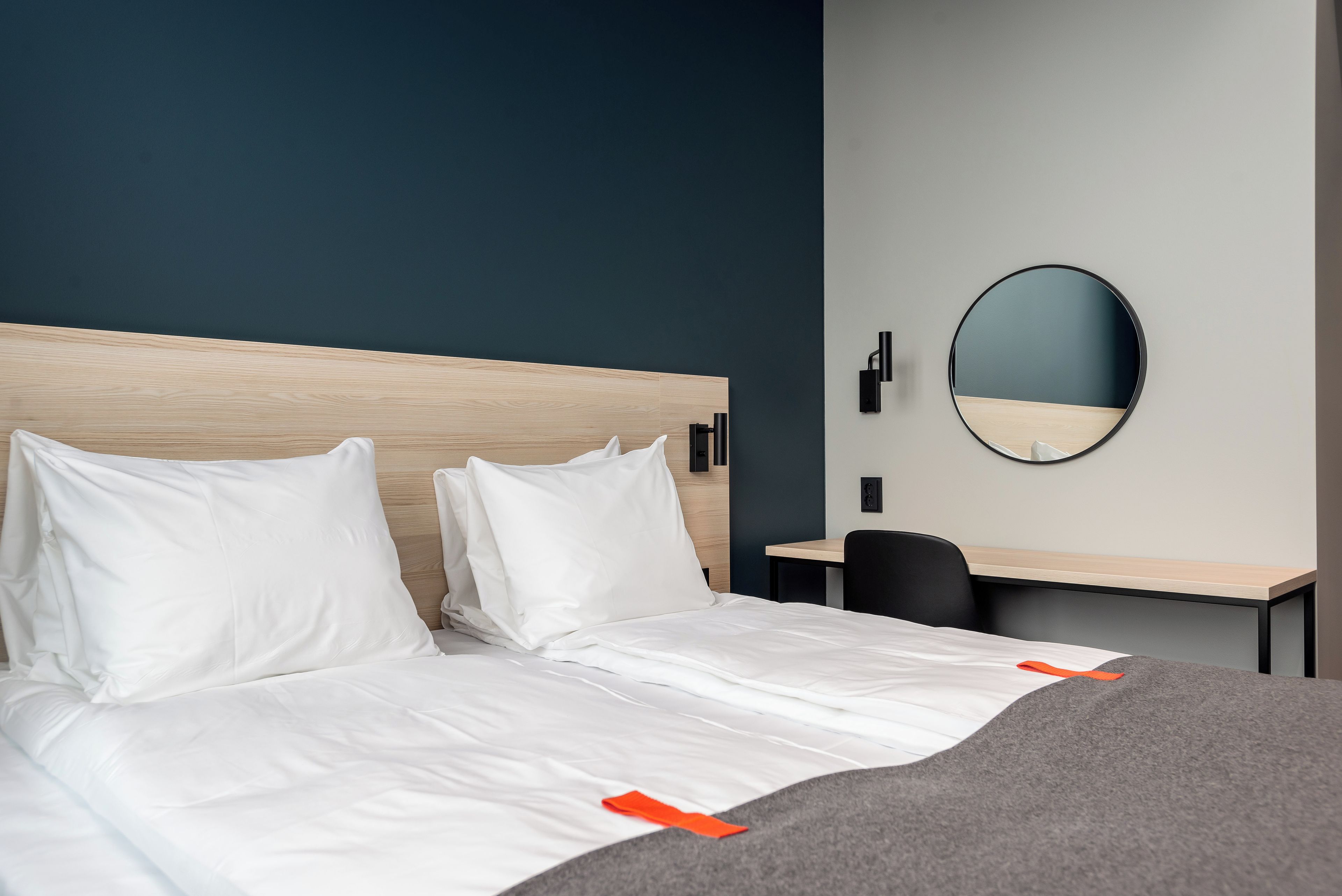 A hotel room with a bed, a desk, and a round mirror on the wall.