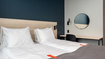 A hotel room with a bed, a desk, and a round mirror on the wall.