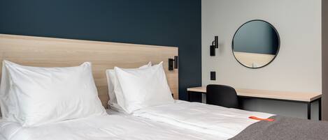A hotel room with a bed, a desk, and a round mirror on the wall.