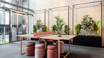 A modern office space with a long table, multiple round ottomans, and potted plants.
