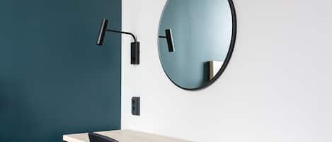 A modern room with a wooden desk, a black chair, a round mirror, and a wall-mounted light fixture.