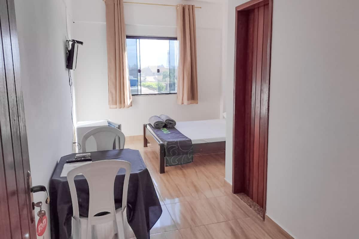 Ein Zimmer mit einem Bett, einem Tisch mit Stühlen, einem Fenster mit Vorhängen und einer Tür.