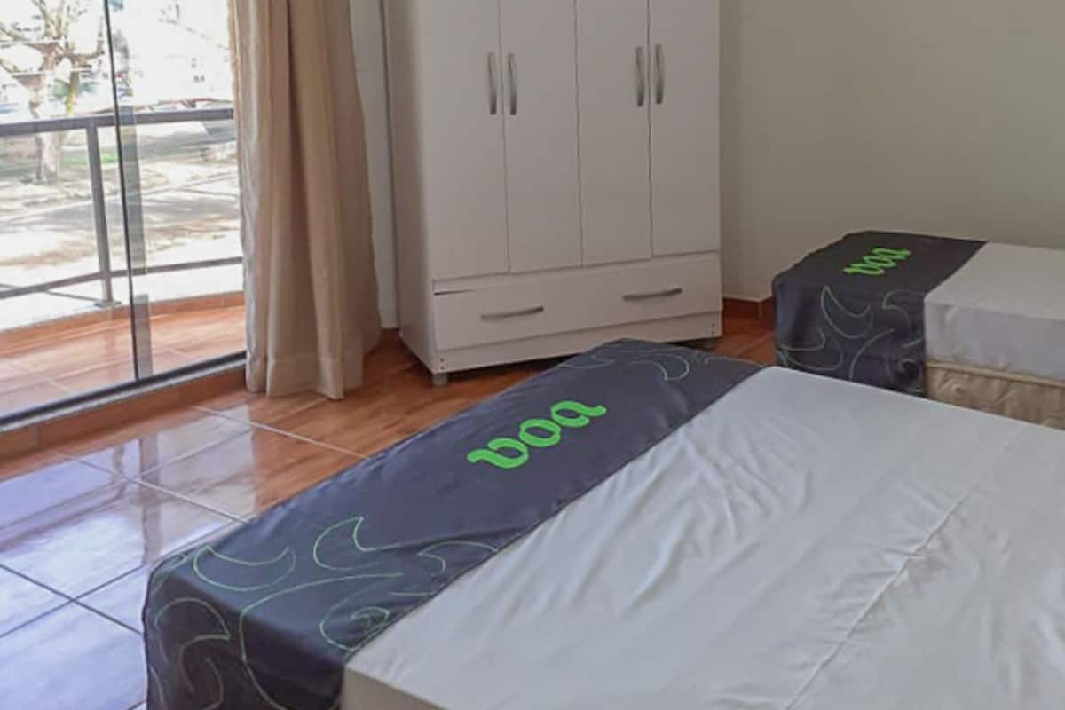 Ein Hotelzimmer mit großem Kleiderschrank, einem Bett mit 'DOO'-Bettdecke, einem Fenster mit Vorhängen und einer Klimaanlage.