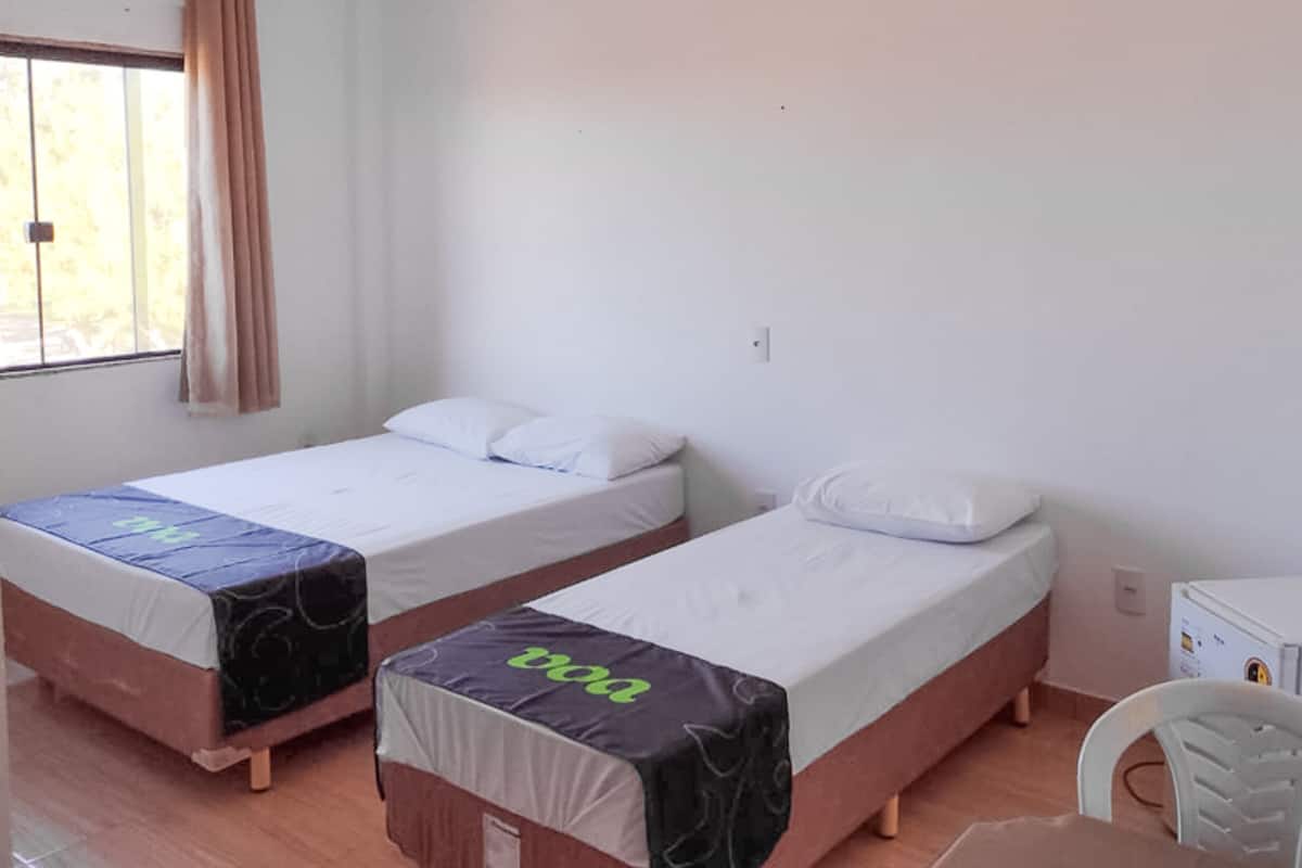 Zwei Einzelbetten mit weißen Bettwäsche und einem Bettbezug in Schwarz und Grün, ein weißer Stuhl und eine kleine weiße Kommode in einem Zimmer mit weißen Wänden und einem Fenster mit Vorhängen.