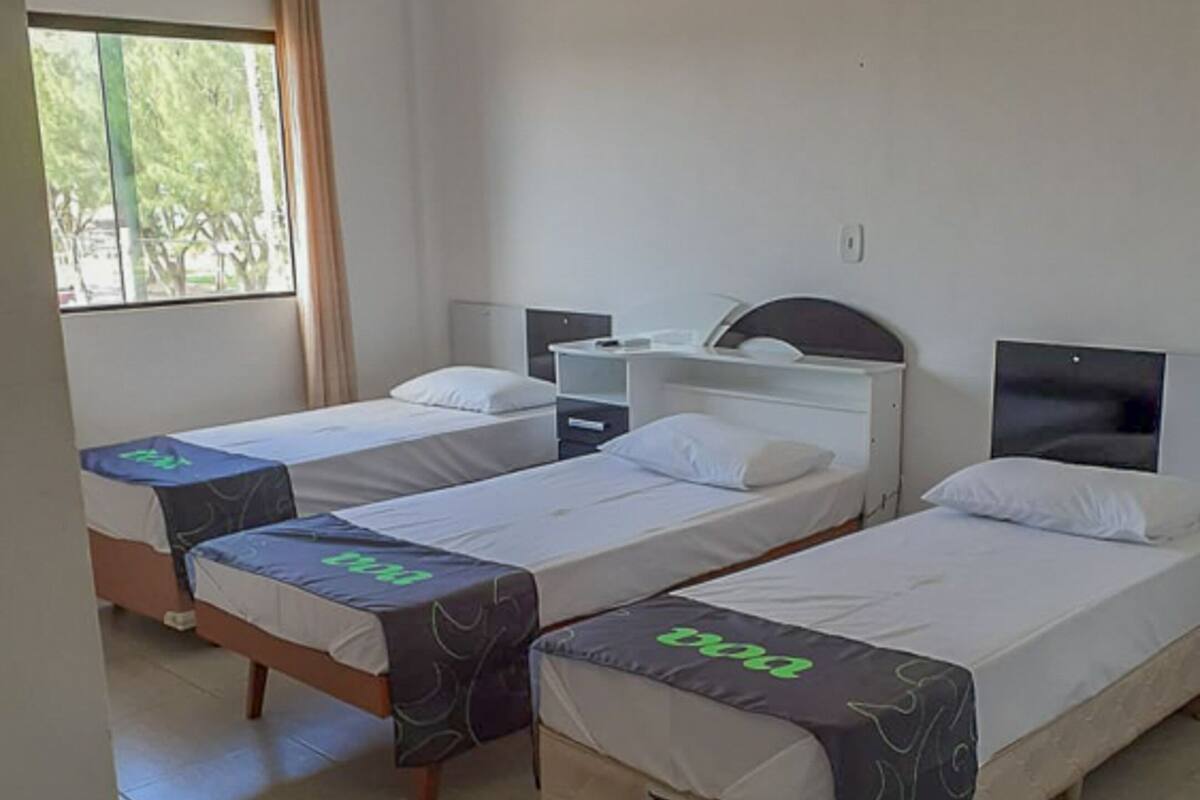 Ein Hotelzimmer mit drei Einzelbetten, einem Schreibtisch und einem Fenster mit Vorhängen.