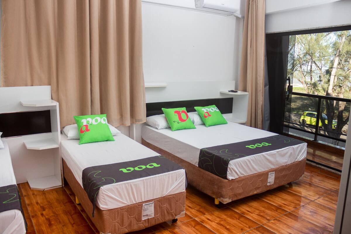 Ein Hotelzimmer mit zwei Betten, jedes mit einer 'boa'-bezogenen Matratze. Links neben den Betten befindet sich ein kleiner Tisch und ein Stuhl, und ein großes Fenster bietet einen Ausblick nach draußen.