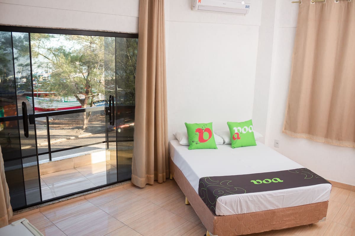 Ein Hotelzimmer mit einem Bett, zwei Kissen, einem Fenster mit Blick auf Boote und einem Vorhang.